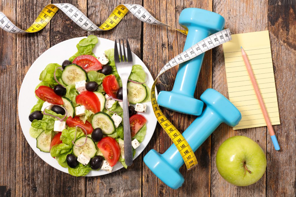 plate of salad, tape measure, green apple and light blue weights.