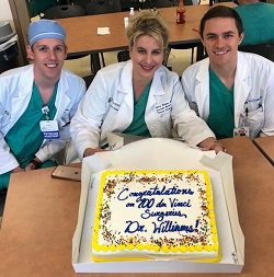 Dr. Williams and two other medical professionals hold a decorated cake for the 100th da Vinci Surgery.