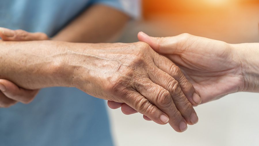 An arthritic person's hand is held by a supporting hand.