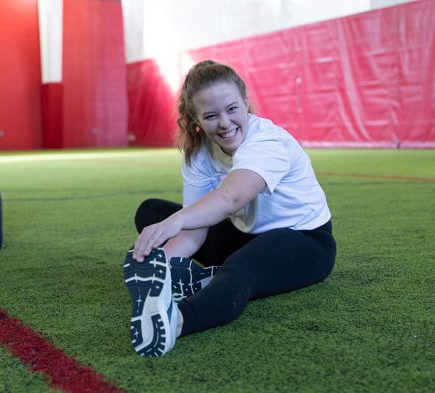 Student Athlete Smiles at the camera while performance a leg stretch.