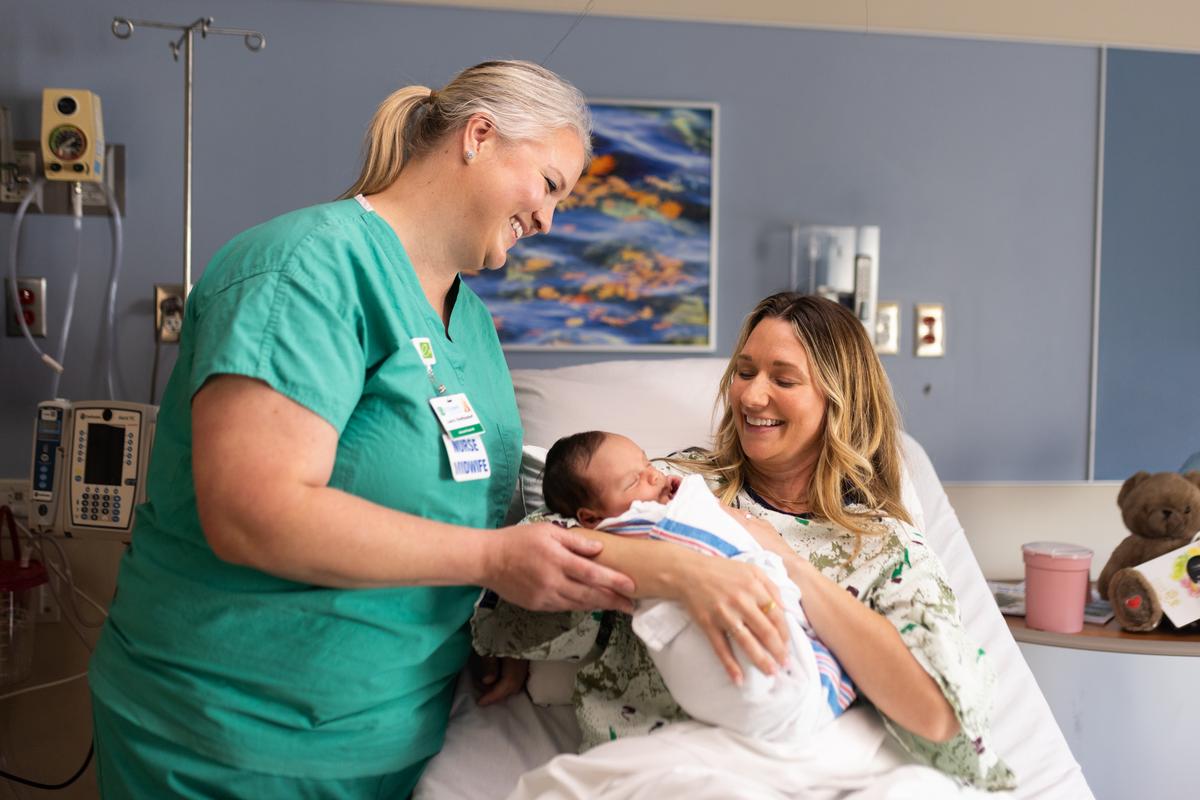 Nurse helps a female patient with her newborn in the hospital. 