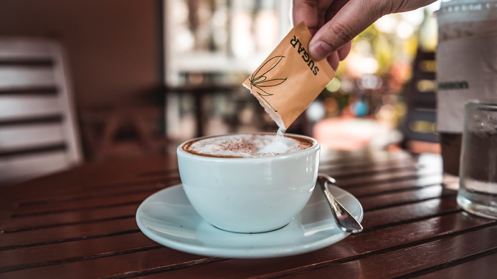 Person pouring sugar packet into coffee