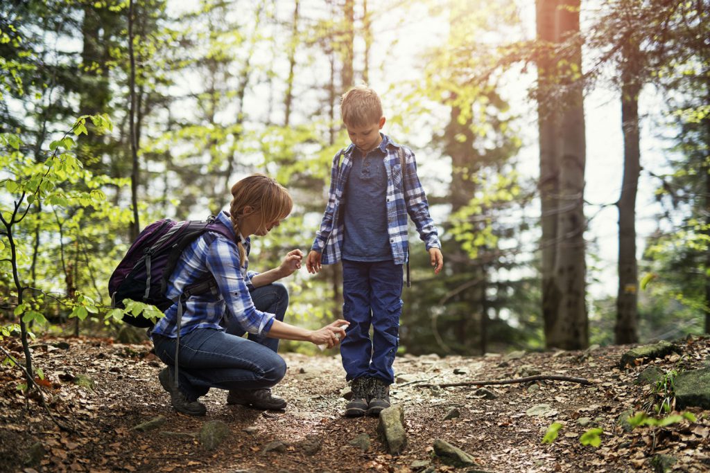 Mother sprays son with insect repellent in the woods