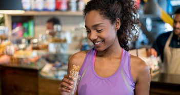 Young African American woman in workout clothes holding granola bar
