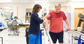Female physical therapist helps male stroke patient walk.