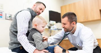 Dr. Philip Hartman working with young boy and his father in doctor's office exam room.