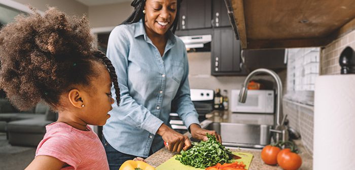 African American mother and daughter cutting vegetables together in kitchen.