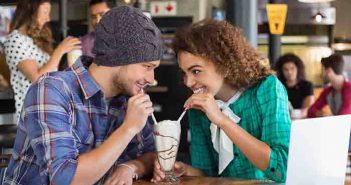Happy couple looking at each other while having milkshake in restaurant