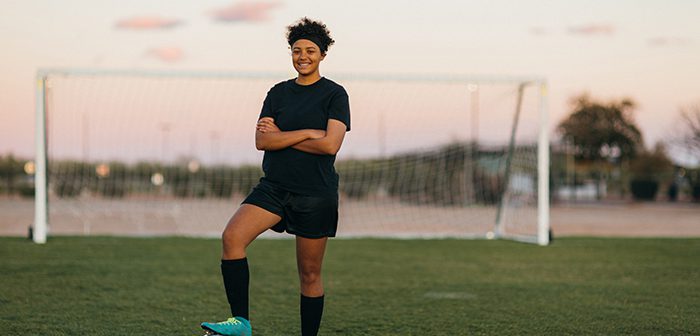 A female high school soccer player in practice uniform poses for a portrait while on the pitch in Arizona, USA. She is a young woman athlete who loves to compete in the sport of soccer.