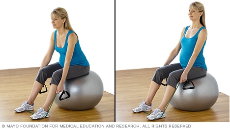 Pregnant person doing a seated dead lift with resistance tubing