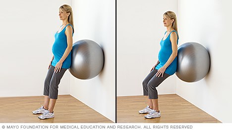 Pregnant person doing squats with a fitness ball