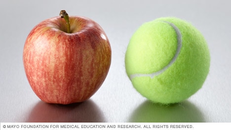 A small apple next to a tennis ball.
