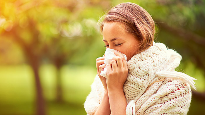 Young girl wearing scarf blowing her nose outdoors.