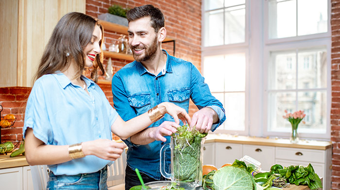 Young, healthy cpuple making green smoothies in brightly lit kitchen.